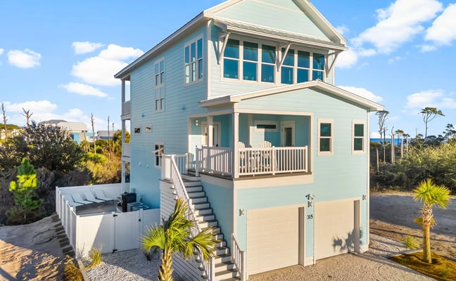 Aerial view of beachfront residential community with white and blue houses, beach access sign, and ocean beyond